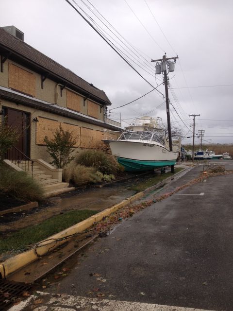 1990 Ford Bronco - A boat rests on land, displaced by storm damage, with a building secured by plywood and power lines down.