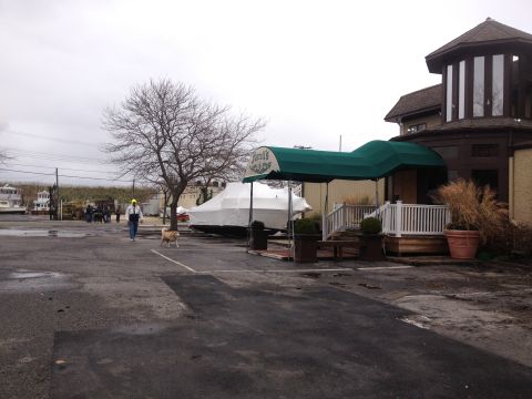 1990 Ford Bronco - A person and dog walk past a boat covered in a white tarp outside a building with a green awning.