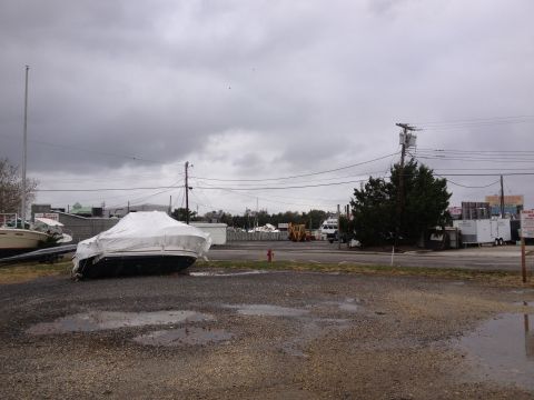 1990 Ford Bronco - A covered boat sits in a lot with other marine vessels and trailers under a cloudy sky.