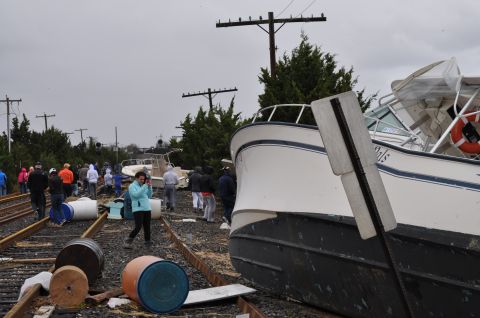 1990 Ford Bronco - A boat rests on train tracks, surrounded by debris and onlookers, likely after a storm.