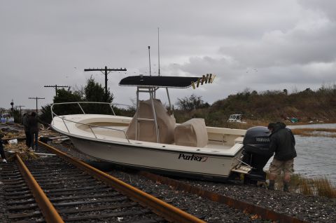1990 Ford Bronco - A boat sits stranded on train tracks near a body of water, with two people observing.