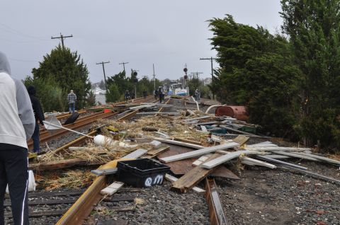 1990 Ford Bronco - Train tracks are covered in debris, with people and a boat visible in the distance after a storm.
