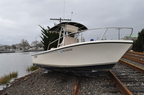 1990 Ford Bronco - A white boat rests on train tracks near a body of water under an overcast sky.