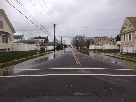 1990 Ford Bronco - A suburban street is submerged in floodwaters under an overcast sky.
