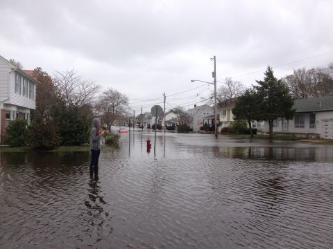 1990 Ford Bronco - A person stands in a flooded suburban street during a storm, with houses lining the road.