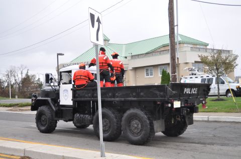 1990 Ford Bronco - A black military truck with police markings and three individuals in life vests is seen on the road.