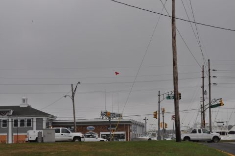 1990 Ford Bronco - Two vehicles are parked near a commercial building with a marina visible behind it under an overcast sky.