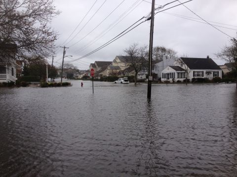 1990 Ford Bronco - A white car is partially submerged in floodwaters on a residential street, indicating severe weather conditions.