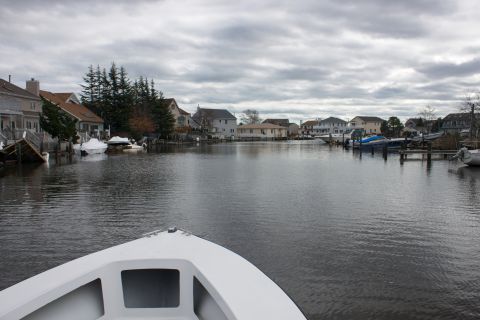 1990 Ford Bronco - A cloudy day scene shows houses and boats along a canal, with the bow of a boat in the foreground.