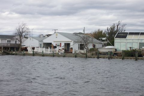 1990 Ford Bronco - Waterfront homes show signs of damage, likely from a storm surge, with debris and structural issues apparent.