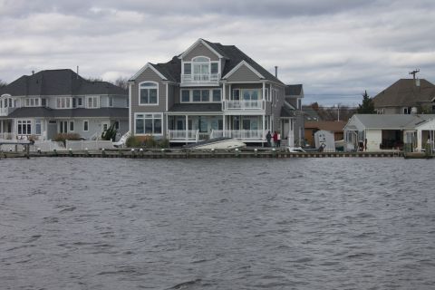 1990 Ford Bronco - Several houses line the waterfront under a cloudy sky, with a damaged boat resting on the shore.