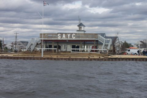 1990 Ford Bronco - A clubhouse with 'SAYC' visible on its facade sits on the waterfront under a cloudy sky.