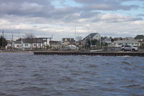 1990 Ford Bronco - A silver SUV is parked on a dock near houses and boats, under a cloudy sky.