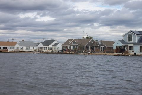 1990 Ford Bronco - Houses line a waterfront, showing signs of damage from flooding under a dramatic sky.