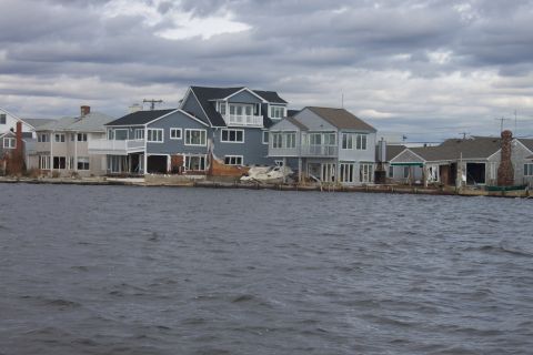 1990 Ford Bronco - Waterfront homes show damage from flooding, with debris scattered along the shore under a stormy sky.