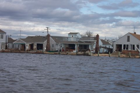 1990 Ford Bronco - Houses damaged by flooding, with water lapping at their foundations under a cloudy sky.