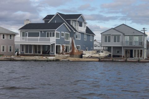 1990 Ford Bronco - A boat lies on land between two houses damaged by flooding, with the water in the foreground.