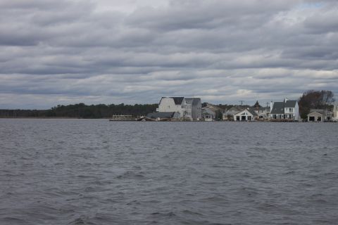 1990 Ford Bronco - Houses line the waterfront under a dramatic, cloudy sky, with choppy water in the foreground.