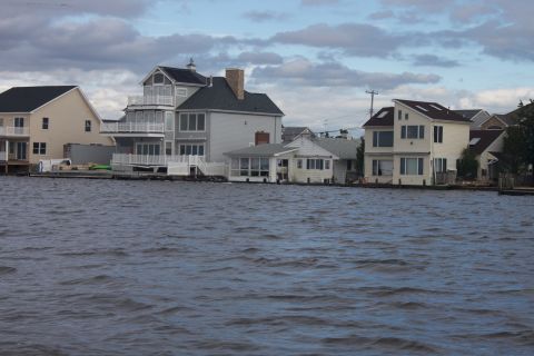1990 Ford Bronco - Waterfront houses line the shore under a cloudy sky, with a watermark from Supermotors.net visible.