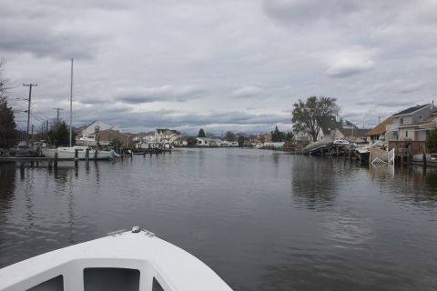 1990 Ford Bronco - View from a boat moving through a canal lined with houses and docked sailboats under a cloudy sky.