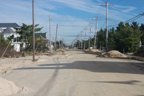 1990 Ford Bronco - A street is covered in sand, with piles of sand on the sides, and houses and power lines lining the road.