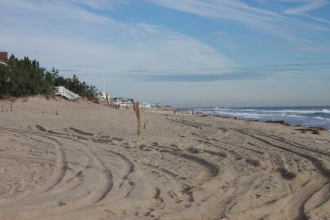 1990 Ford Bronco - Tire tracks mark the sandy beach leading to the ocean under a partly cloudy sky.