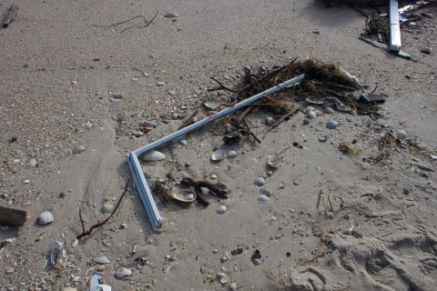 1990 Ford Bronco - Debris litters a sandy beach, with a metal frame and seaweed among shells and driftwood.