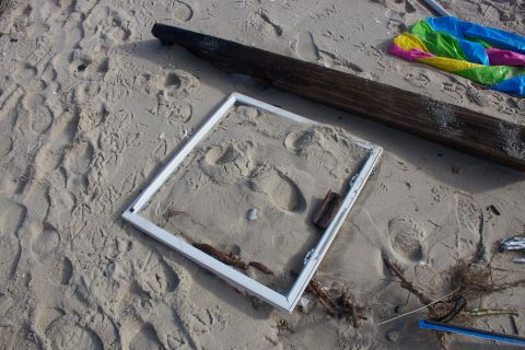 1990 Ford Bronco - Debris litters a sandy beach, including a wooden beam, a discarded picture frame, and a deflated inflatable toy.