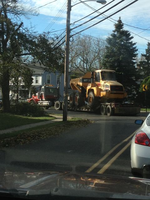 1990 Ford Bronco - A yellow articulated dump truck is transported on a flatbed trailer by a red semi-truck on a street.