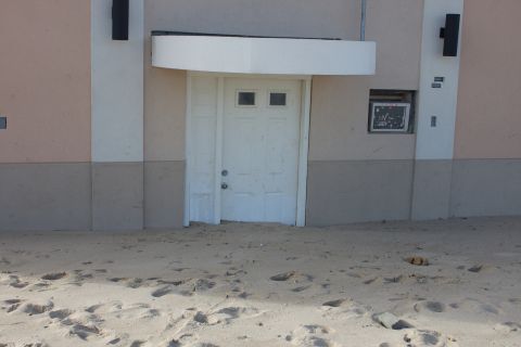 1990 Ford Bronco - A building entrance is partially buried in sand, suggesting a significant environmental event like a storm.