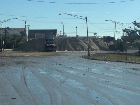 1990 Ford Bronco - A truck with a snow plow is positioned in front of large piles of sand, with construction equipment visible in the distance.