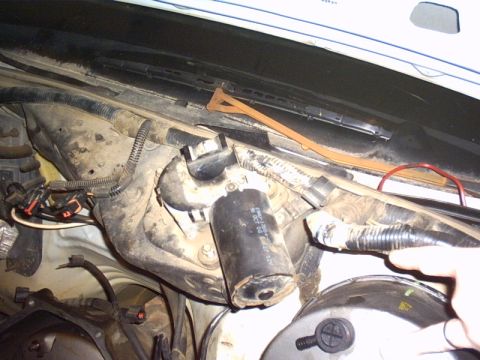 1991 Ford LTD Crown Victoria - Close-up under an open hood at the cowl, showing the black windshield wiper motor and linkage mounted to the firewall, with a date-coded la…