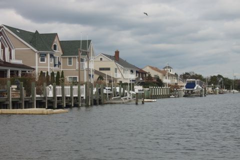 1990 Ford Bronco - A boat is parked on a trailer next to a dock, with houses lining the waterfront under a cloudy sky.