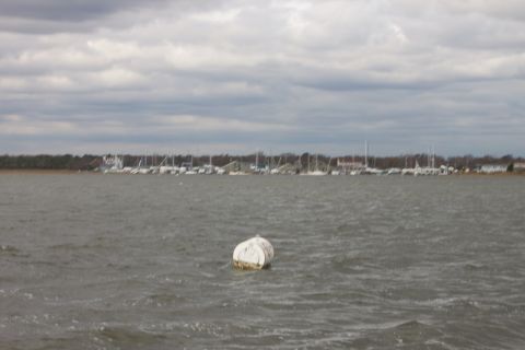 1990 Ford Bronco - A solitary buoy bobs in the choppy water, with a distant marina visible under a cloudy sky.