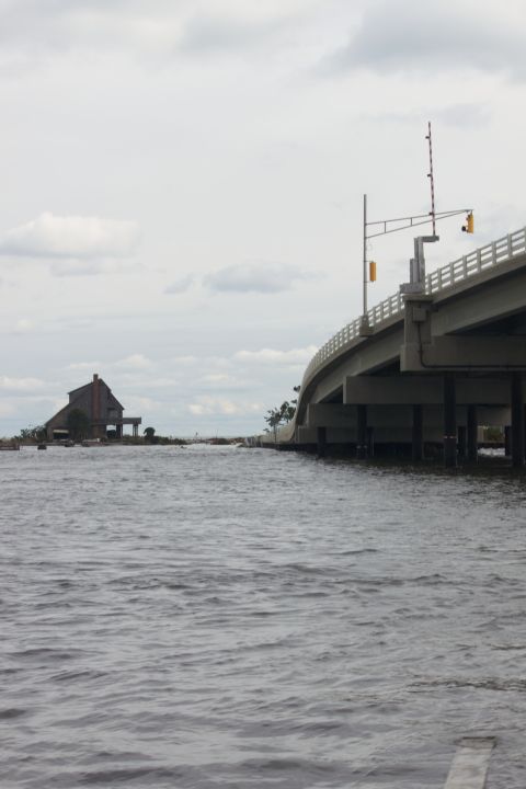1990 Ford Bronco - A bridge arches over choppy water, with a weathered building visible on a distant shore.