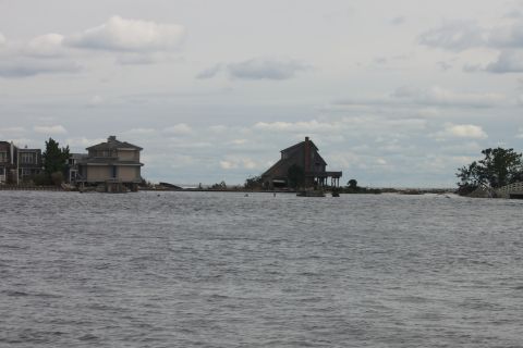 1990 Ford Bronco - Coastal houses stand on stilts, some appearing damaged, under an overcast sky.