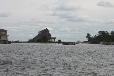1990 Ford Bronco - Waterfront properties with elevated structures stand against a cloudy sky, with debris visible in the distance.