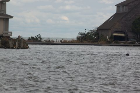 1990 Ford Bronco - A waterfront scene shows damaged houses and debris after a storm, with choppy water in the foreground.