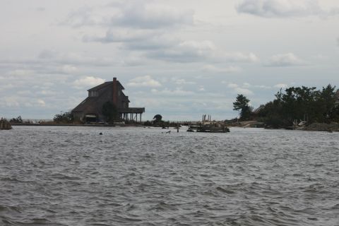 1990 Ford Bronco - A house stands on stilts surrounded by water, with debris scattered around the shore.