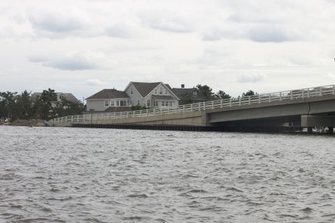 1990 Ford Bronco - A bridge spans a body of water, with houses visible on the shoreline under an overcast sky.