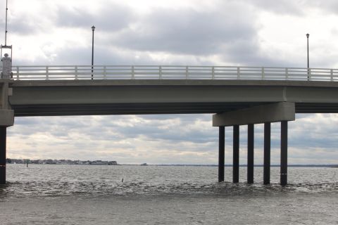 1990 Ford Bronco - A bridge spans a body of water under a cloudy sky, with a distant shoreline visible.