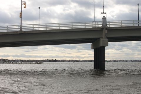 1990 Ford Bronco - A bridge spans over a body of water, with a distant town visible on the horizon under an overcast sky.