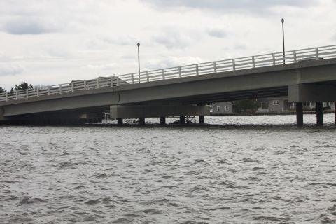 1990 Ford Bronco - A concrete bridge spans over choppy water under a cloudy sky, with houses visible on the far bank.