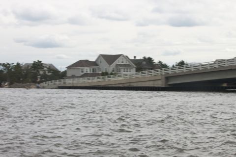 1990 Ford Bronco - A bridge spans a body of water, with houses visible on the shore under an overcast sky.