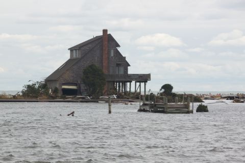 1990 Ford Bronco - A house on stilts stands in floodwaters, showing signs of damage and debris from a storm.