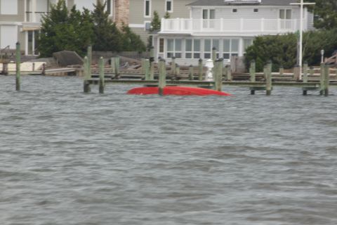 1990 Ford Bronco - A red boat is submerged and overturned in the water near a pier, with houses in the background.
