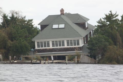 1990 Ford Bronco - A house on stilts appears damaged by floodwaters, with trees and a wooden dock visible nearby.
