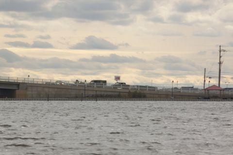 1990 Ford Bronco - Multiple vehicles are seen driving on a bridge that spans over a body of water under a cloudy sky.