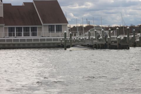 1990 Ford Bronco - A boat is partially submerged in the water next to a wooden dock, with a building visible behind it.