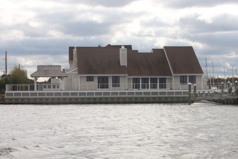 1990 Ford Bronco - A boat is partially submerged next to a dock, with a large house and cloudy sky visible.